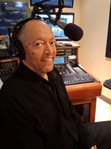 WSGE DJ Special T, Wearing a dark shirt, smiling in control room.